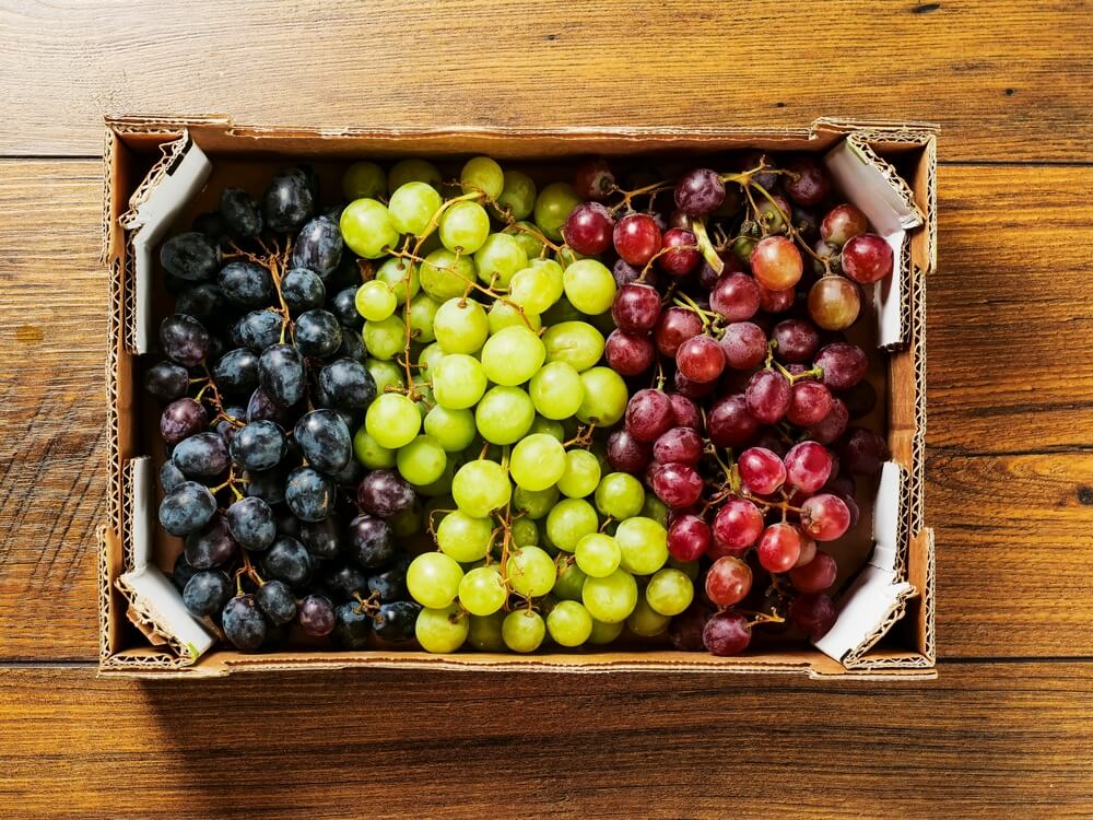 Três uvas de diferentes cores dentro de uma caixa.