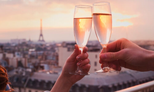 Duas Pessoas Brindando Em Paris, Com A Torre Eifel Ao Fundo, Com Espumante, Um Dos Vinhos Da França